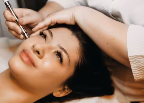 Side view portrait of a cute woman doing microdermabrasion with derma pen on her face in a wellness center.
