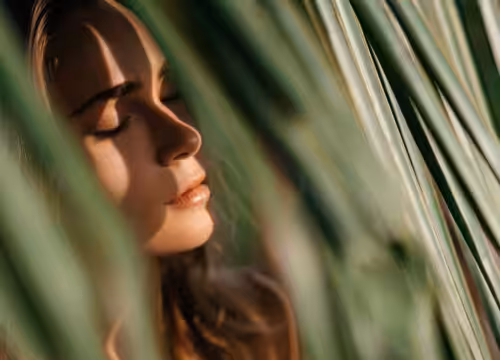 Woman shading herself from the sun with palm leaves