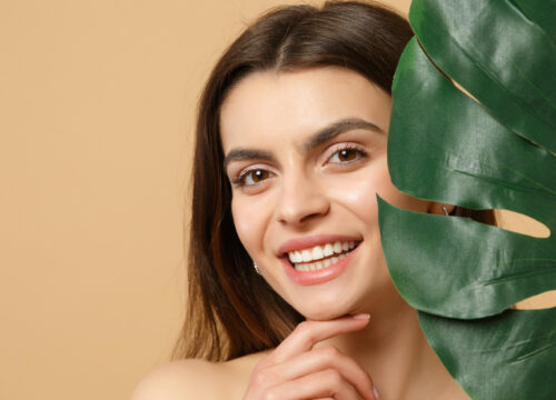 Photo of a woman with great skin smiling next to a palm leaf